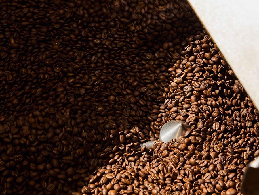 Close-up view of freshly roasted coffee beans being mixed in a roasting machine, with light highlighting the rich brown tones of the beans.